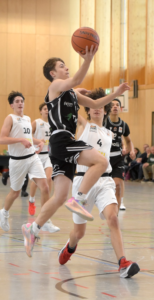Junger Basketballspieler im schwarzen Trikot springt mit konzentriertem Blick zum Korb