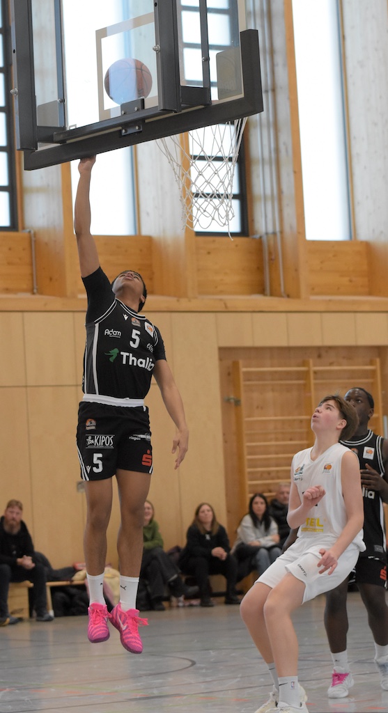 Ein Basketballspieler im schwarzen Trikot springt freudig für einen Korbleger hoch