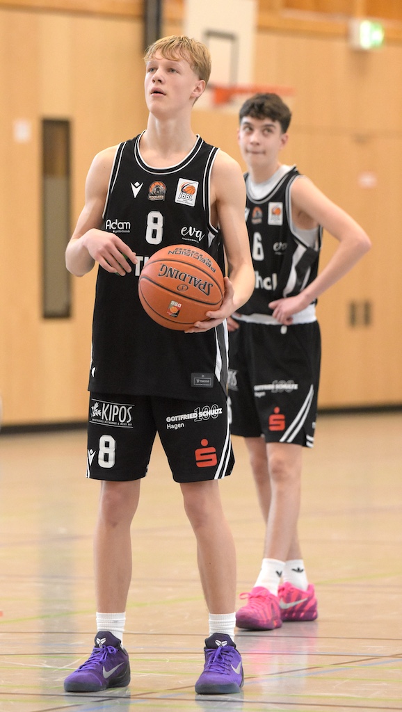 Ein jugendlicher Basketballspieler mit konzentriertem Blick hält einen orangefarbenen Ball
