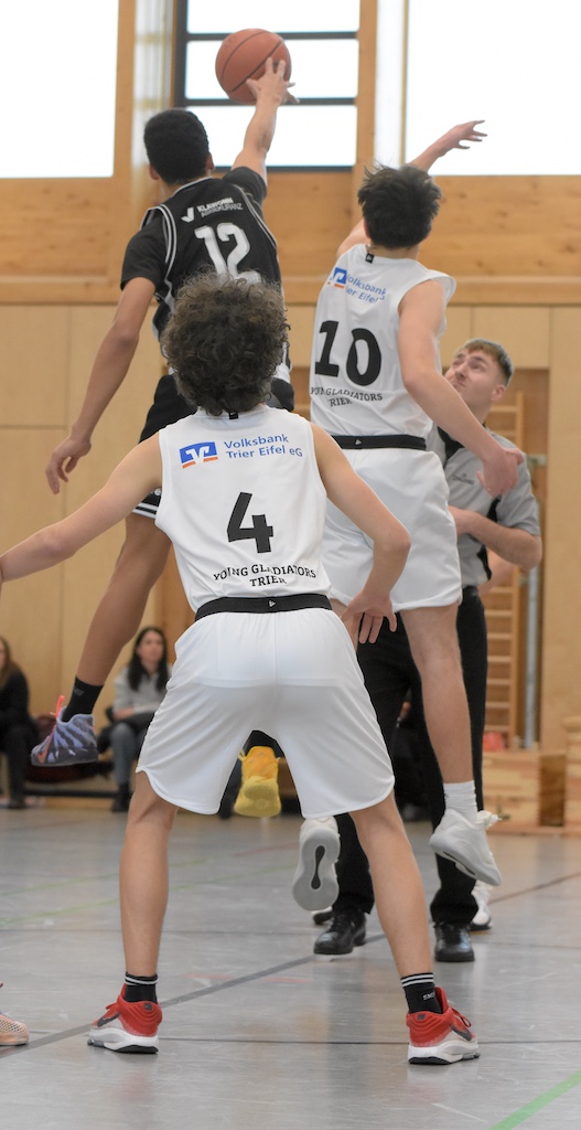 Drei männliche Basketballspieler mit schwarzen und weißen Trikots beim Sprungwurf in heller Sporthalle