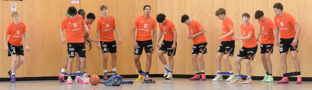 Eine Gruppe junger Männer in orangefarbenen Trikots wirkt konzentriert beim Teambuilding