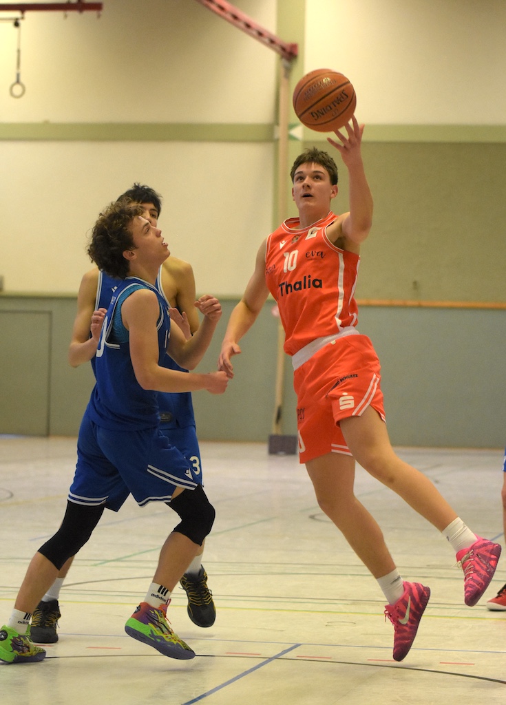 Ein junger Basketballspieler im orangen Trikot springt energisch zum Korb