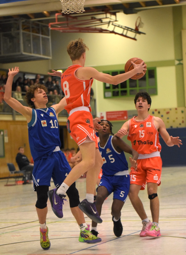 Vier junge Basketballspieler in blauen und orangenen Trikots kämpfen dynamisch um den Ball