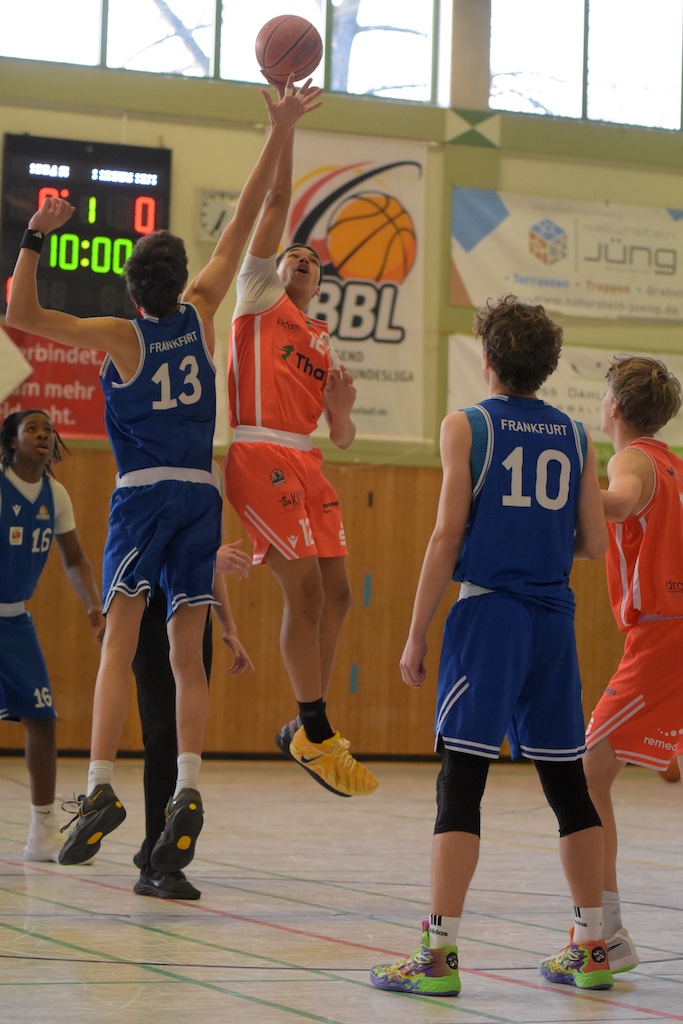 Zwei Jugendliche springen beim Basketballspiel in einer Sporthalle hoch zum Ball