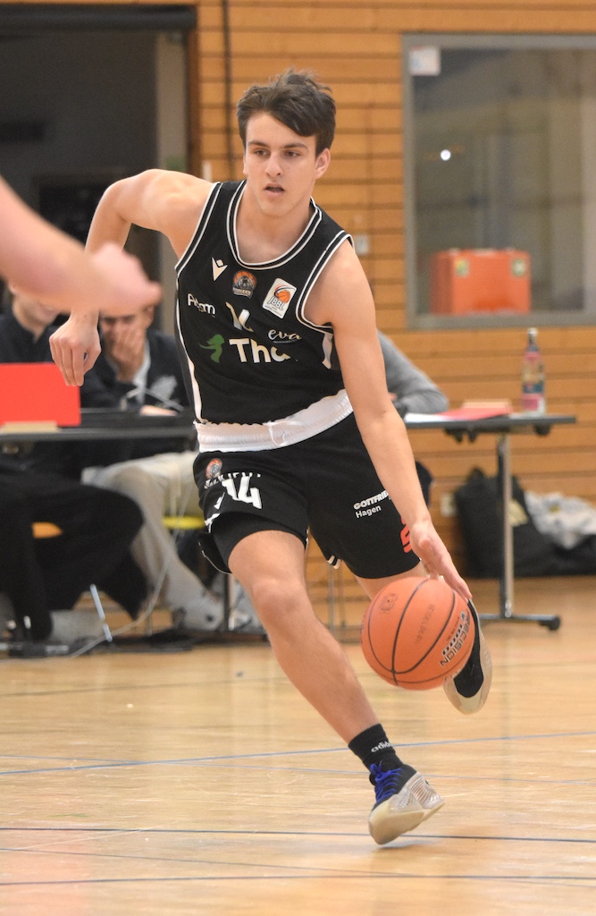 Ein junger Basketballspieler mit konzentriertem Gesichtsausdruck dribbelt den Ball in einer Sporthalle