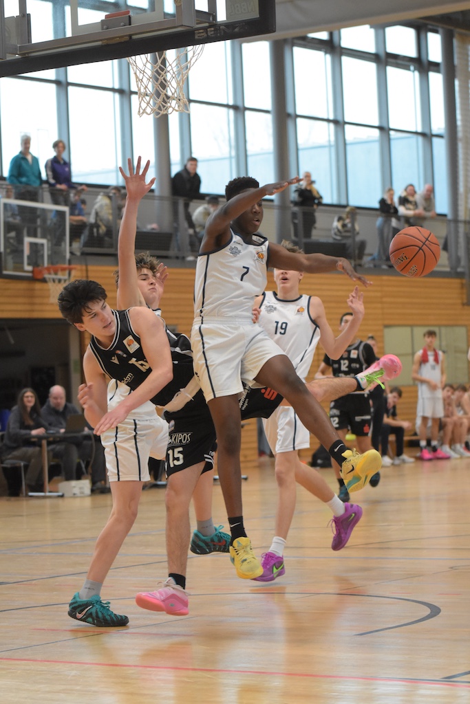 Mehrere junge Basketballspieler in Aktion, einer springt mit konzentriertem Blick zum Ball