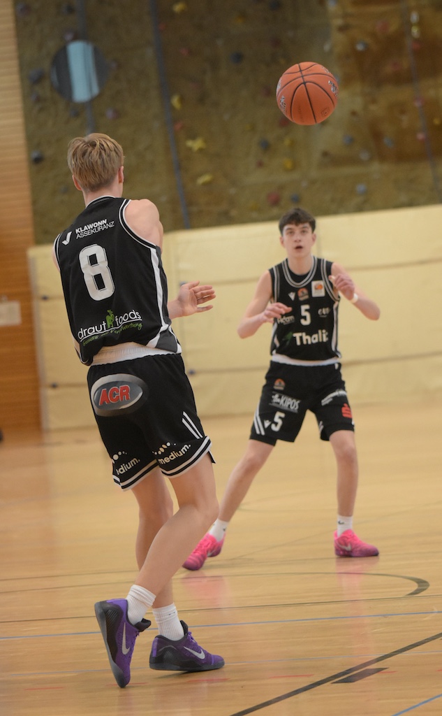 Zwei junge Basketballspieler in schwarzen Trikots passen sich konzentriert den Ball zu