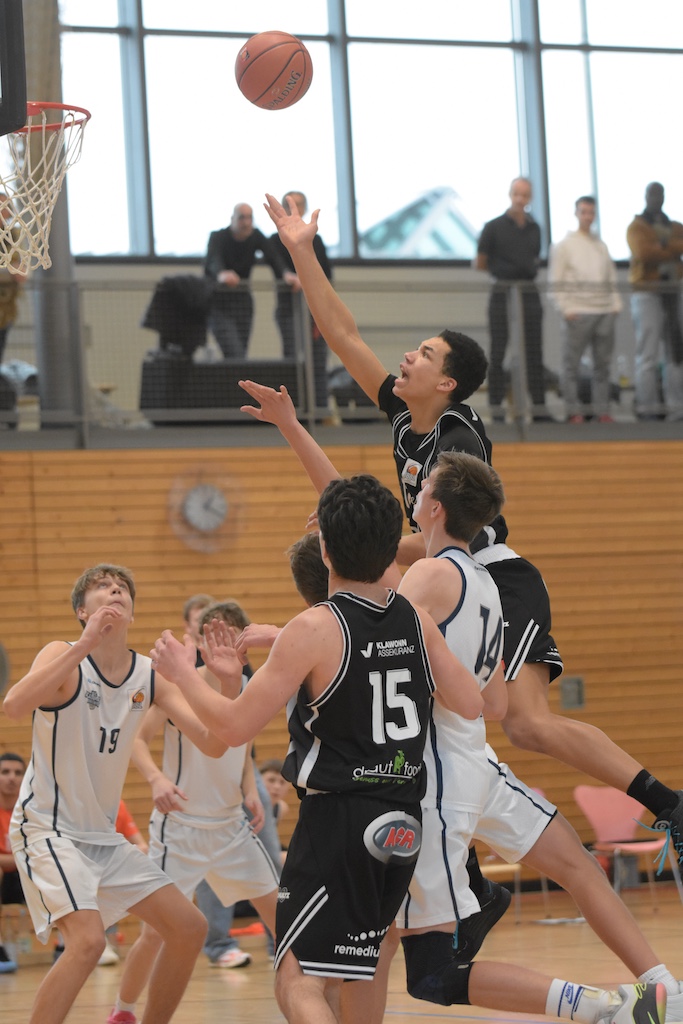 Ein junger Basketballspieler im schwarzen Trikot springt fokussiert zum Korb