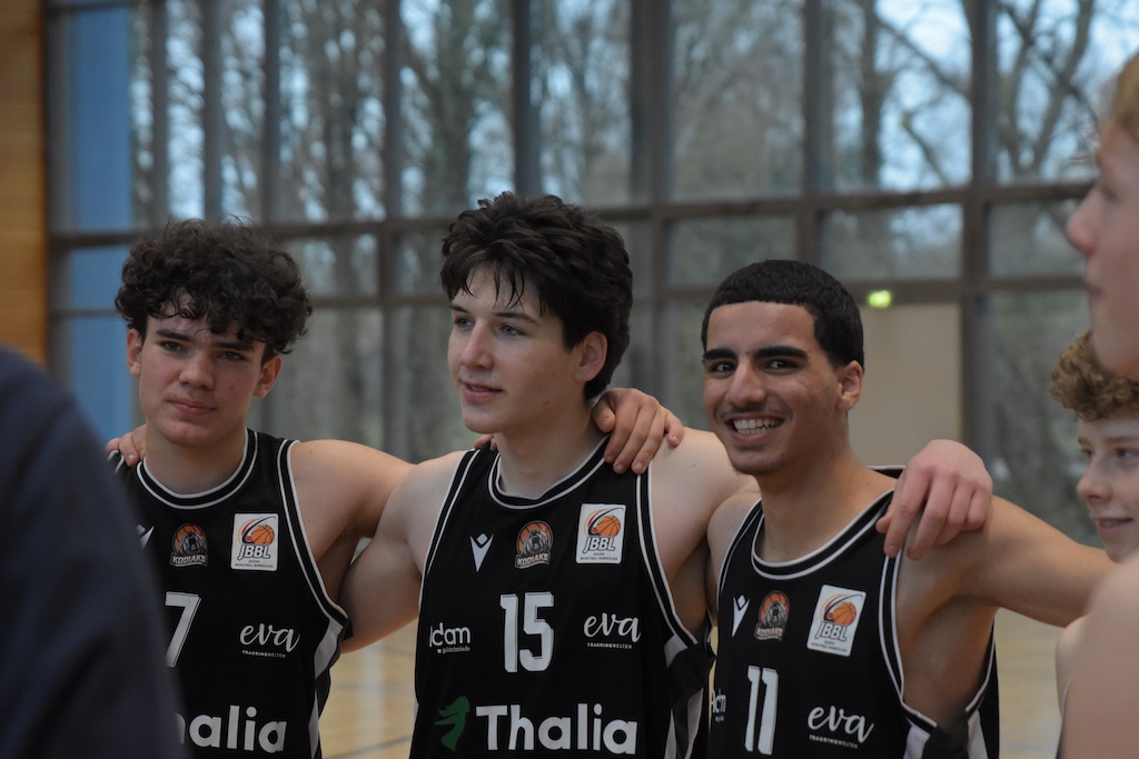 Drei junge Basketballspieler in schwarzen Trikots mit Nummern lächeln zufrieden