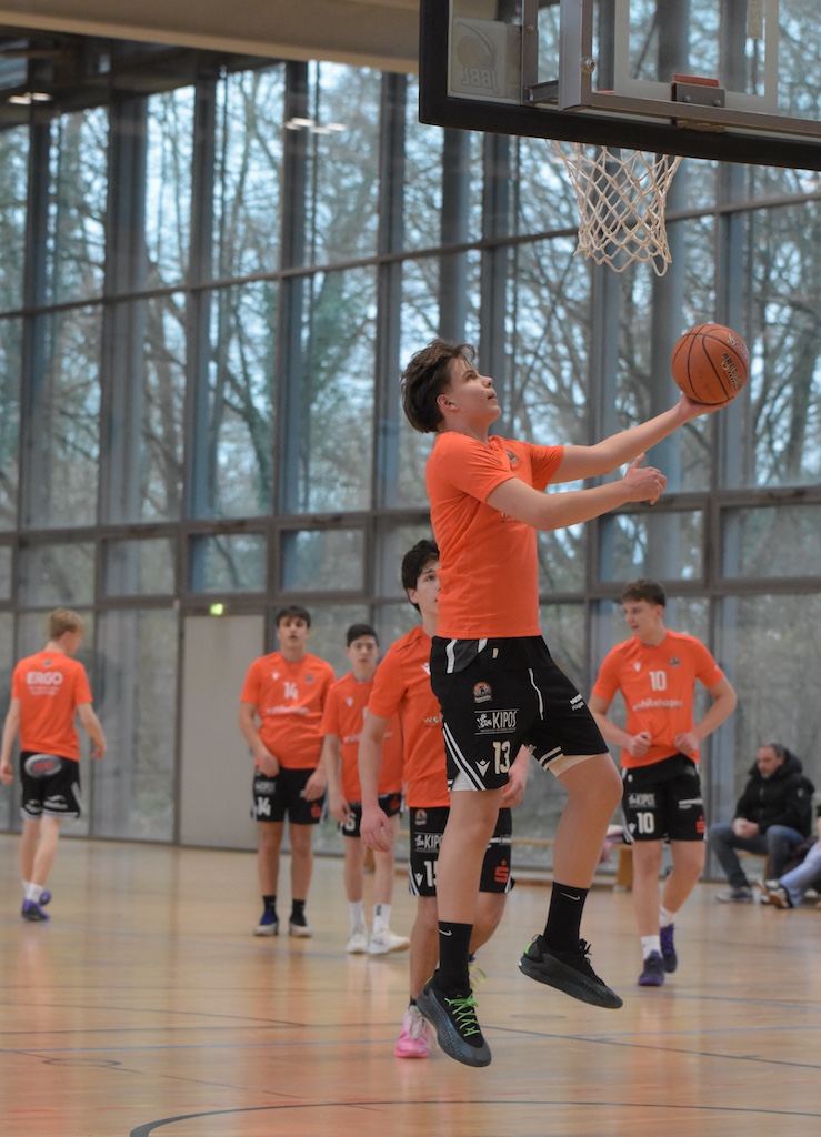 Ein junger Basketballspieler mit konzentriertem Blick macht einen Korbleger in der Halle