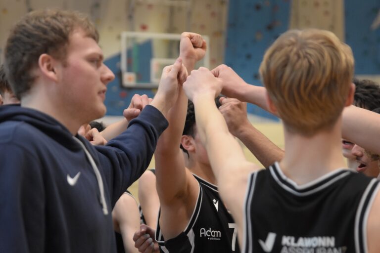 Mehrere junge Basketballspieler in schwarzen Trikots schließen motiviert die Fäuste zusammen