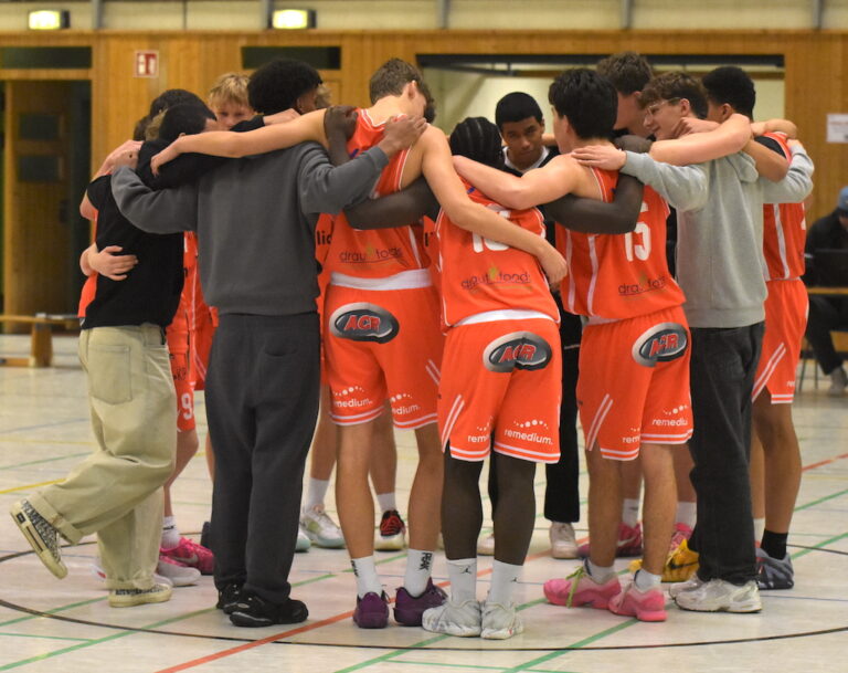 Eine Gruppe junger Basketballspieler in orangenen Trikots umarmt sich im Kreis