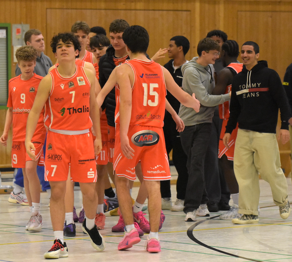 Mehrere junge Basketballspieler im orangefarbenen Trikot jubeln gemeinsam in einer Halle