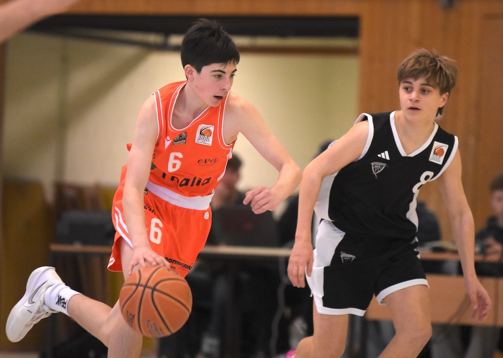 Zwei jugendliche Basketballspieler im Spiel, einer in Orange konzentriert am Dribbeln