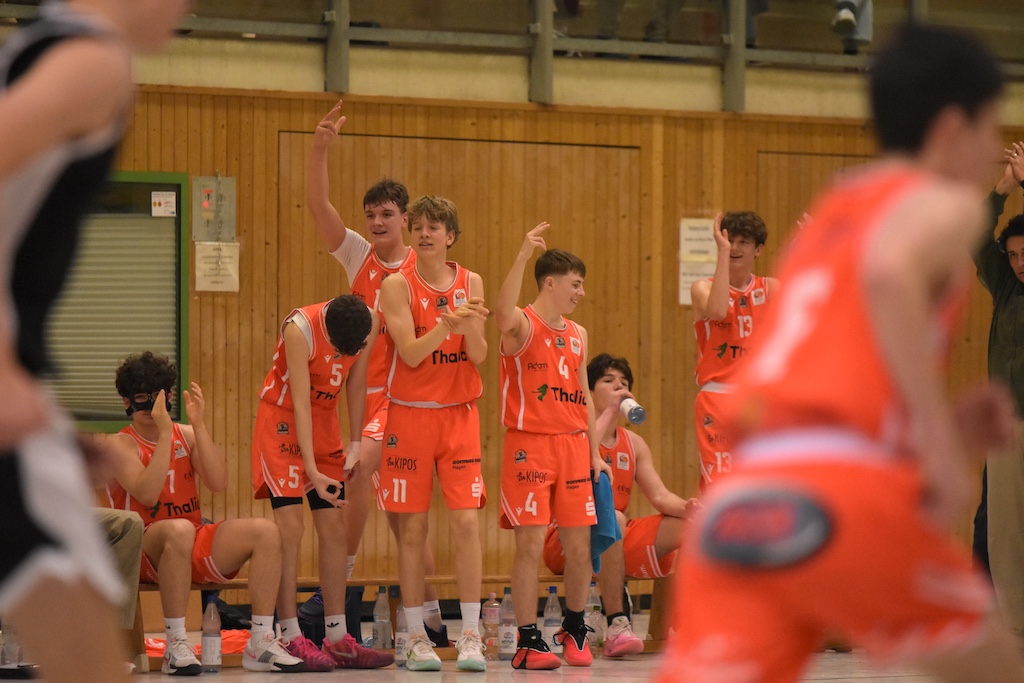 Mehrere Basketballspieler jubeln fröhlich auf der Bank in auffälligen orangen Trikots