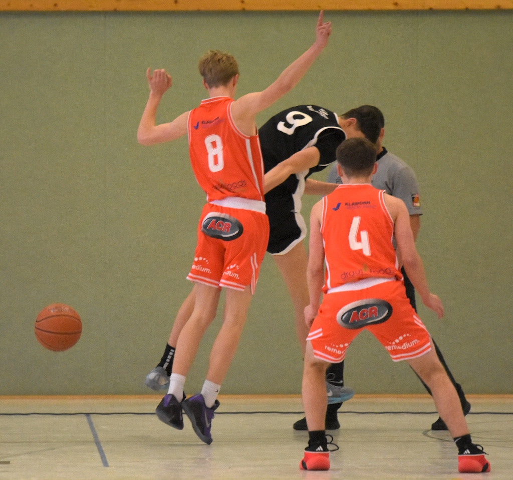 Drei Basketballspieler in orange und schwarz kämpfen dynamisch um den Ball im Spiel
