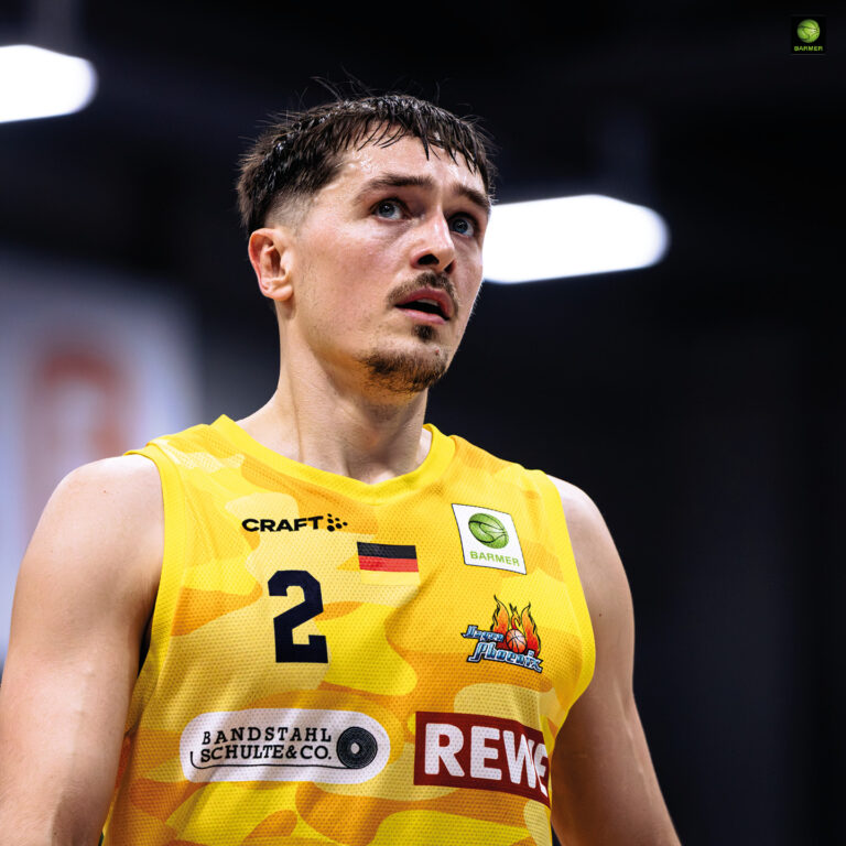Ein Basketballspieler im gelben Trikot mit konzentriertem Blick und kurzen dunklen Haaren