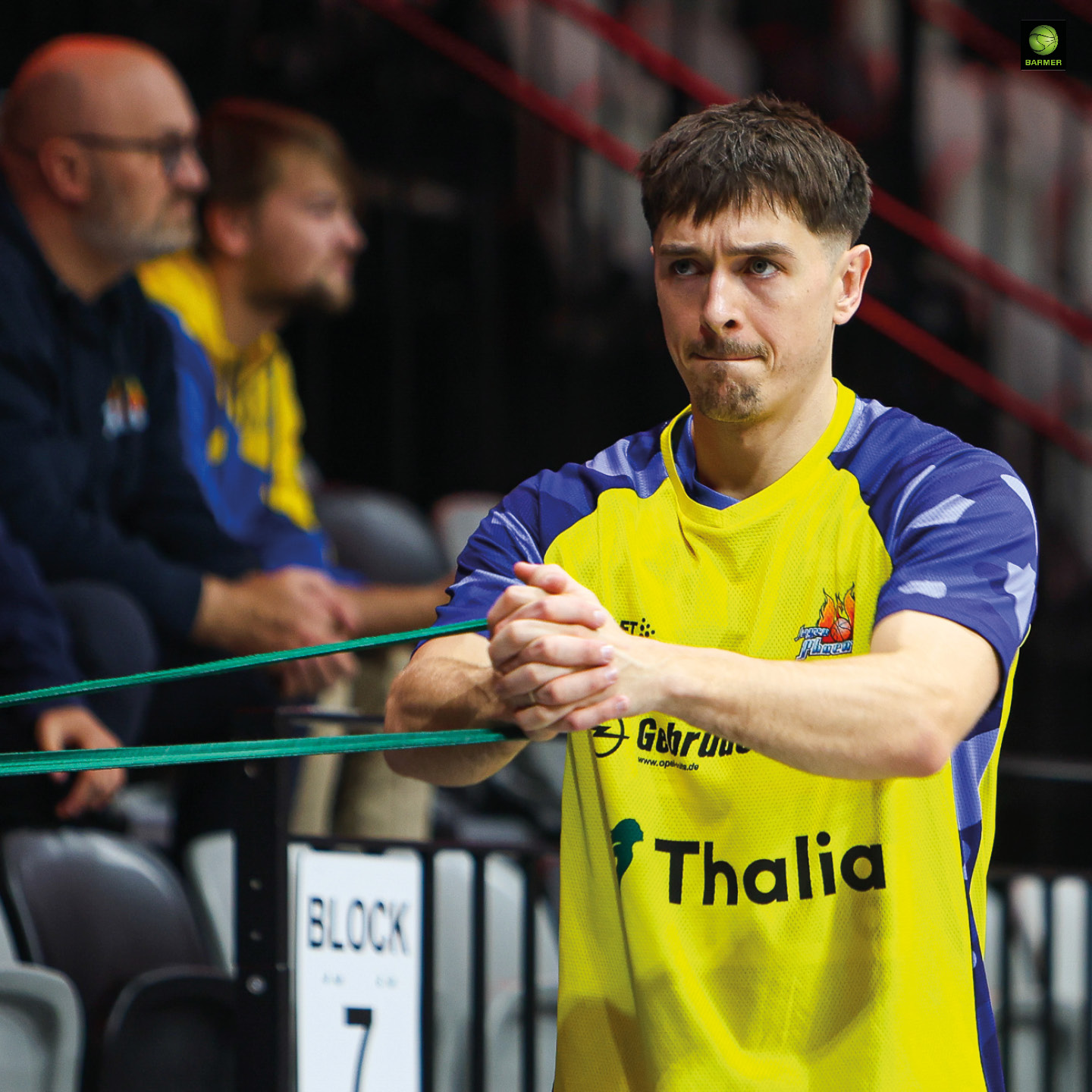 Ein konzentrierter junger Mann im gelben Trikot steht mit verschränkten Händen in der Halle