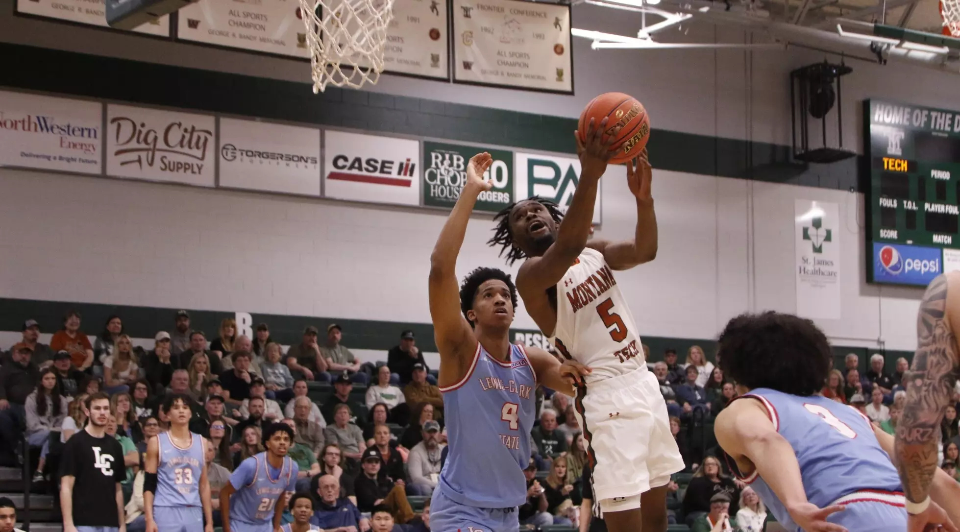 Ein Basketballspieler im weißen Trikot springt entschlossen zum Korb, während ihn Gegner blocken