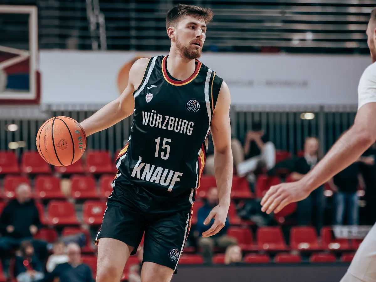 Ein Basketballspieler im schwarzen Trikot mit ernster Miene führt den Ball auf dem Spielfeld