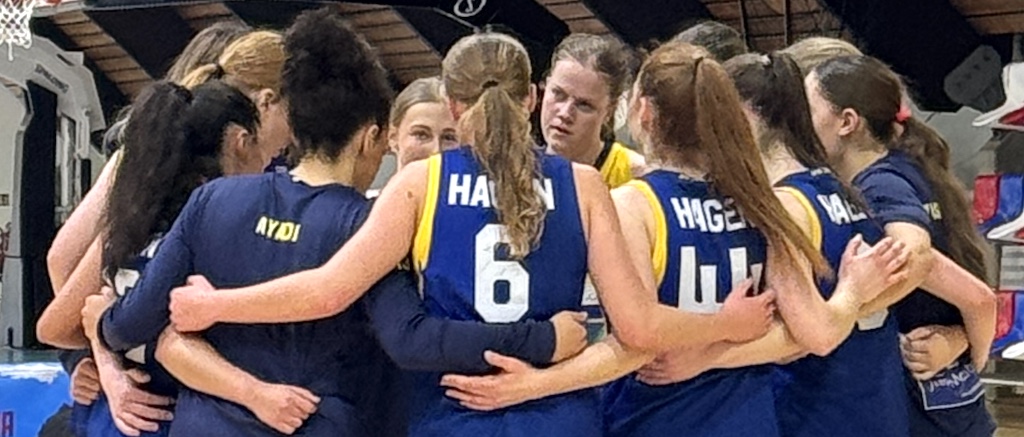 Mehrere Basketballspielerinnen im blauen Trikot umarmen sich motivierend im Kreis