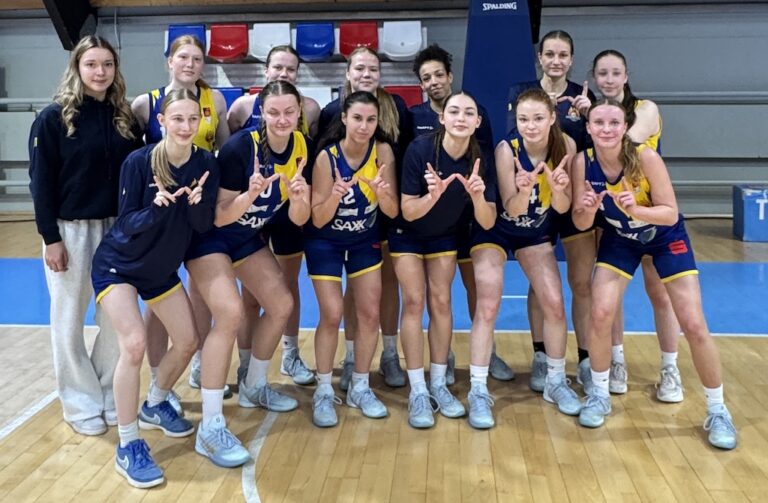 Eine Damen Basketballmannschaft in blau-gelben Trikots lächelt stolz in die Kamera