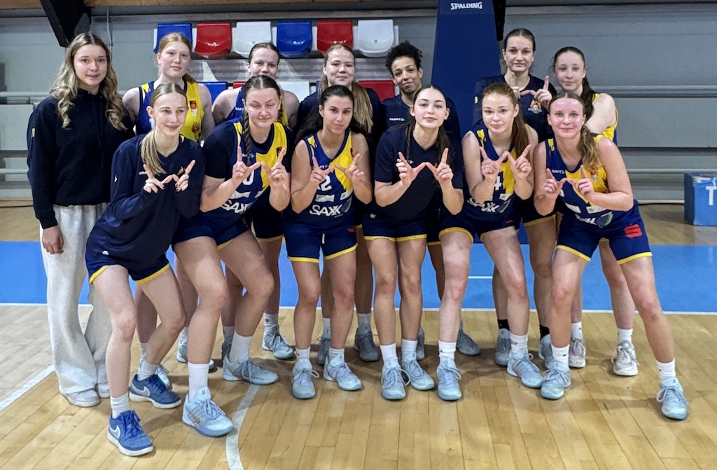 Eine Damen Basketballmannschaft in blau-gelben Trikots lächelt stolz in die Kamera