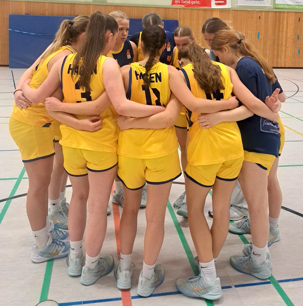 Eine Damen Volleyballmannschaft in gelben Trikots umarmt sich motivierend im Kreis