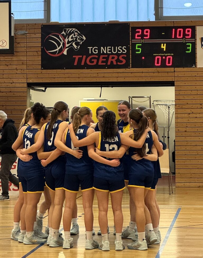 Eine Gruppe junger Basketballspielerinnen im blauen Trikot steht lachend im Kreis