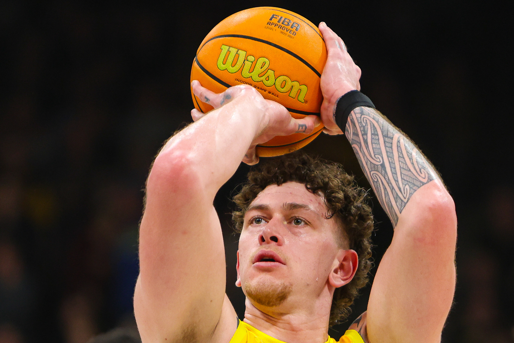 Ein Basketballspieler mit gelbem Trikot schaut konzentriert beim Wurf auf den Ball