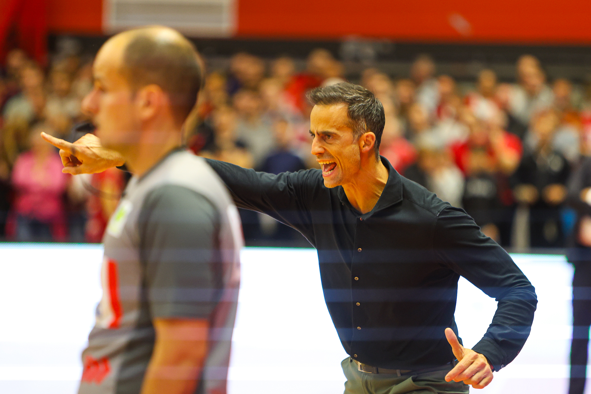 Ein dunkelhaariger Mann in schwarzem Hemd ruft energisch und zeigt nach vorne