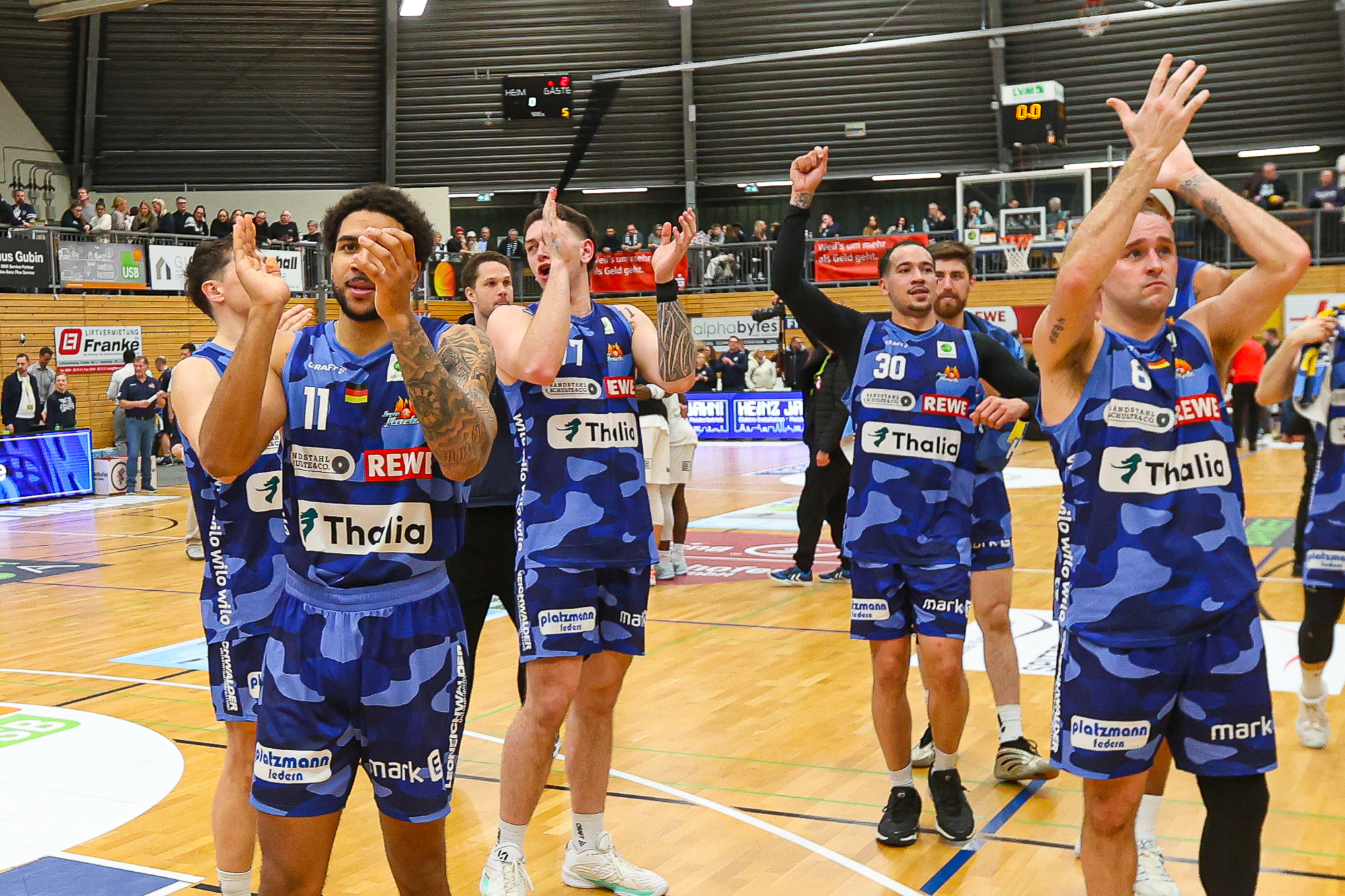 Mehrere Basketballspieler im blauen Trikot klatschen jubelnd auf dem Spielfeld