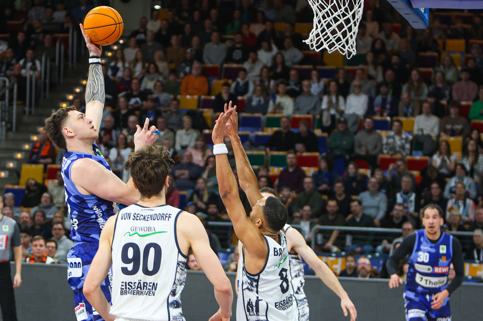 Ein Basketballspieler im blauen Trikot springt entschlossen zum Korb hoch