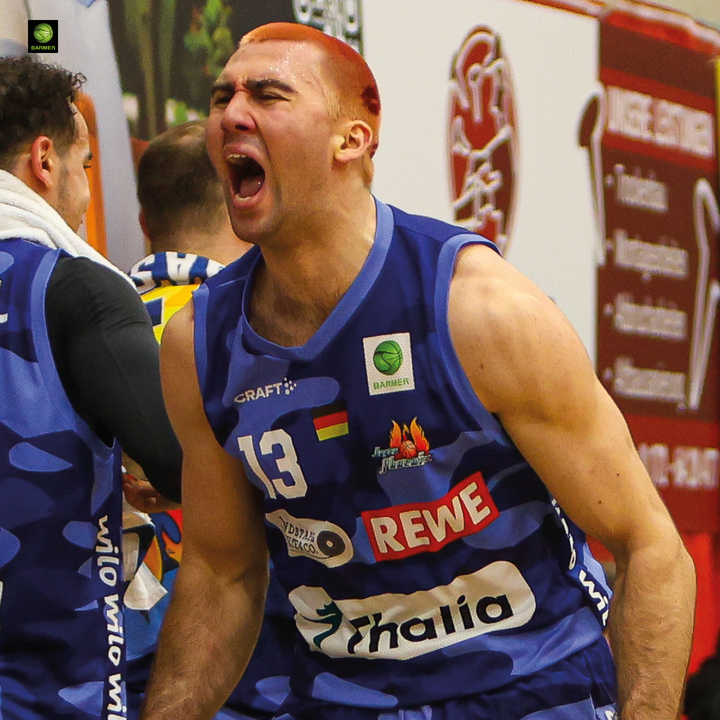 Ein Basketballspieler mit kurz rasierten roten Haaren jubelt leidenschaftlich im blauen Trikot