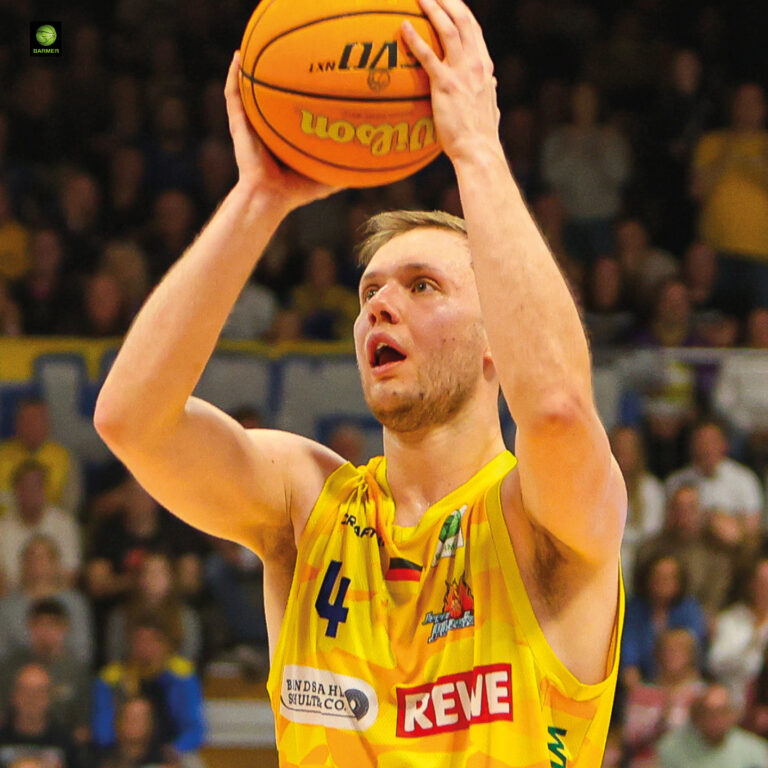 Ein konzentrierter Basketballspieler im gelben Trikot bereitet sich auf einen Wurf vor