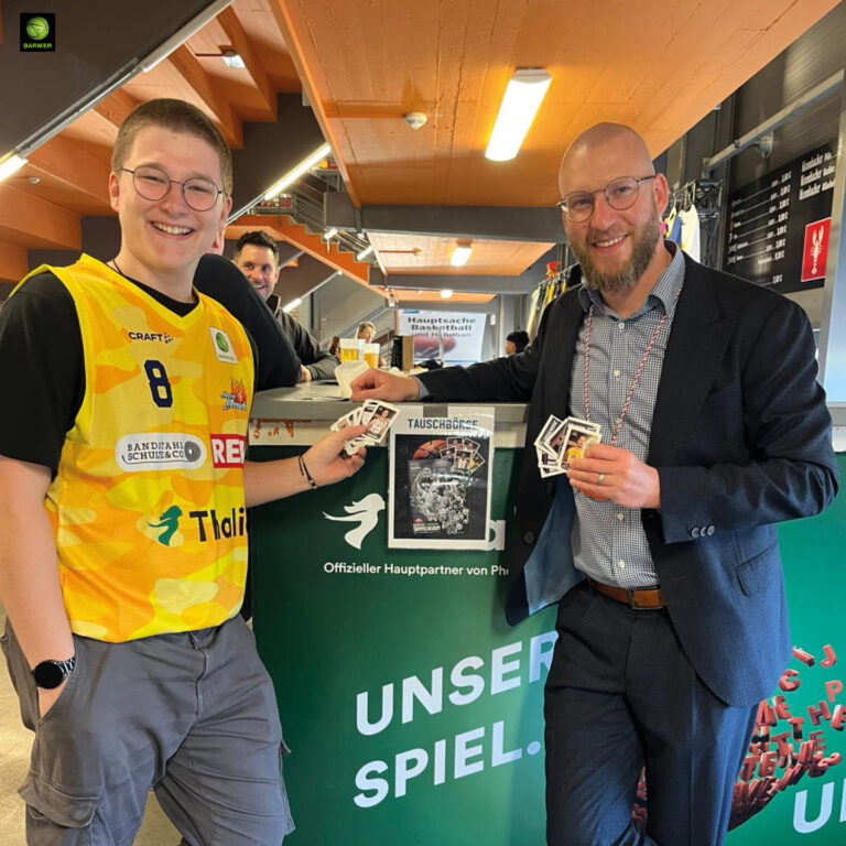 Zwei Männer mit freundlichen Gesichtern halten Sticker an einem grünen Infostand