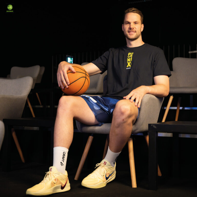 Ein junger Mann mit einem freundlichen Lächeln sitzt mit einem Basketball auf einem Stuhl
