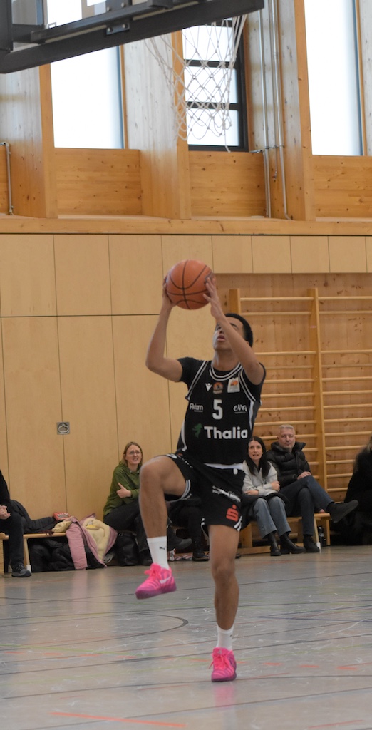 Ein Basketballspieler in schwarzem Trikot mit auffälligen pinken Schuhen springt zum Korbleger