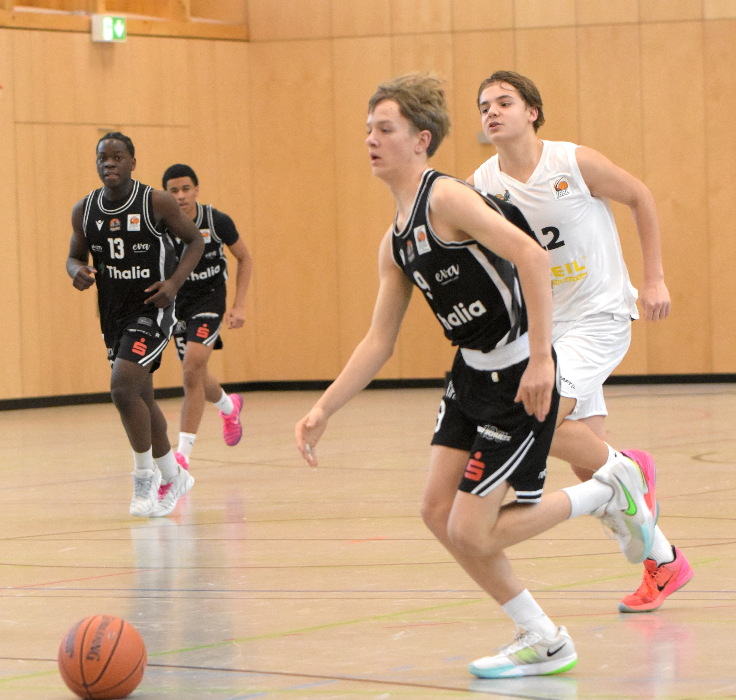 Junger Basketballspieler mit entschlossenem Gesichtsausdruck dribbelt den Ball in heller Halle