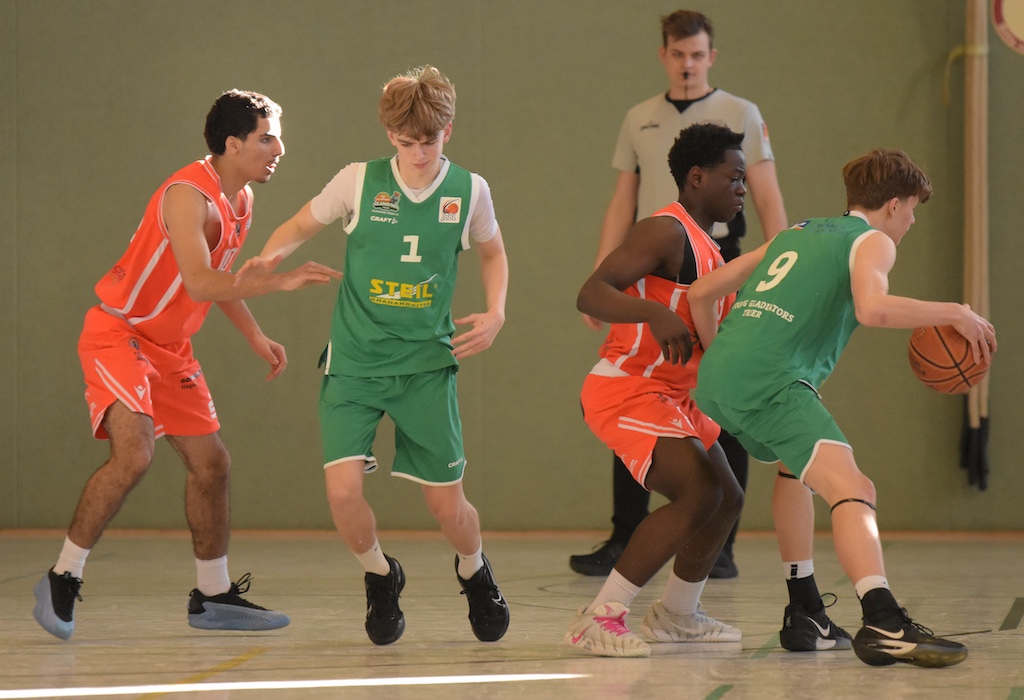 Vier junge Basketballspieler im Spiel, einer dribbelt konzentriert den Ball im Sonnenlicht