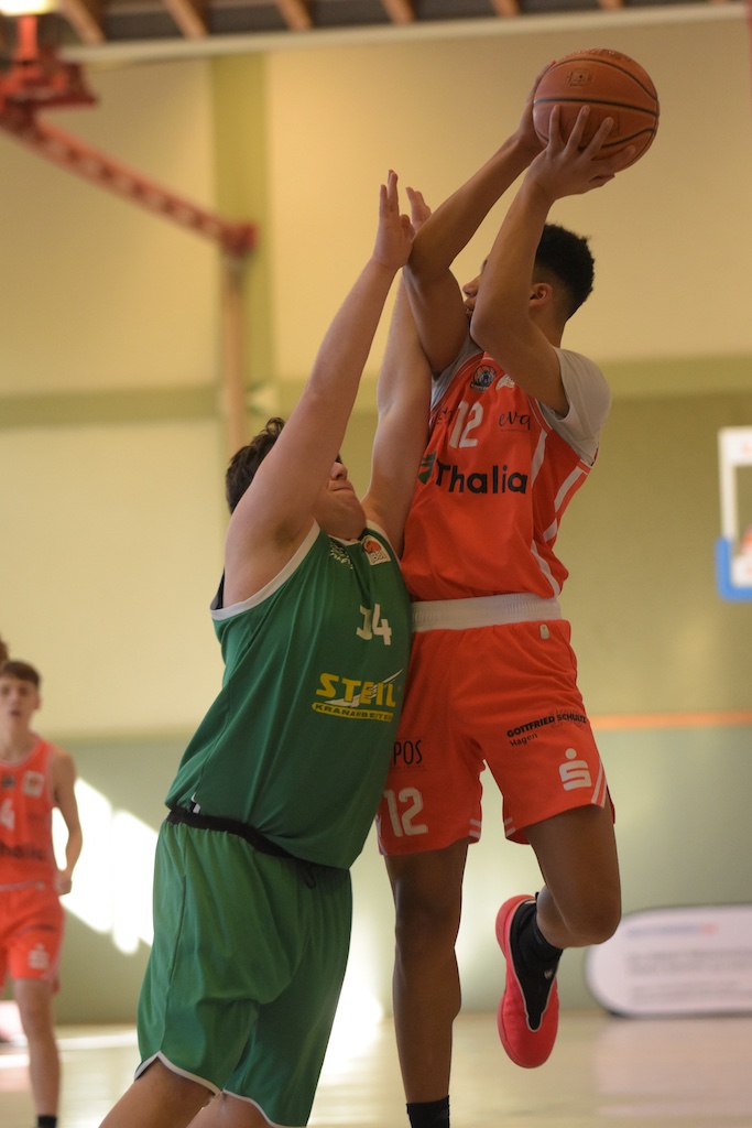 Zwei Basketballspieler kämpfen im Spiel um den Ball, einer in Grün und einer in Orange