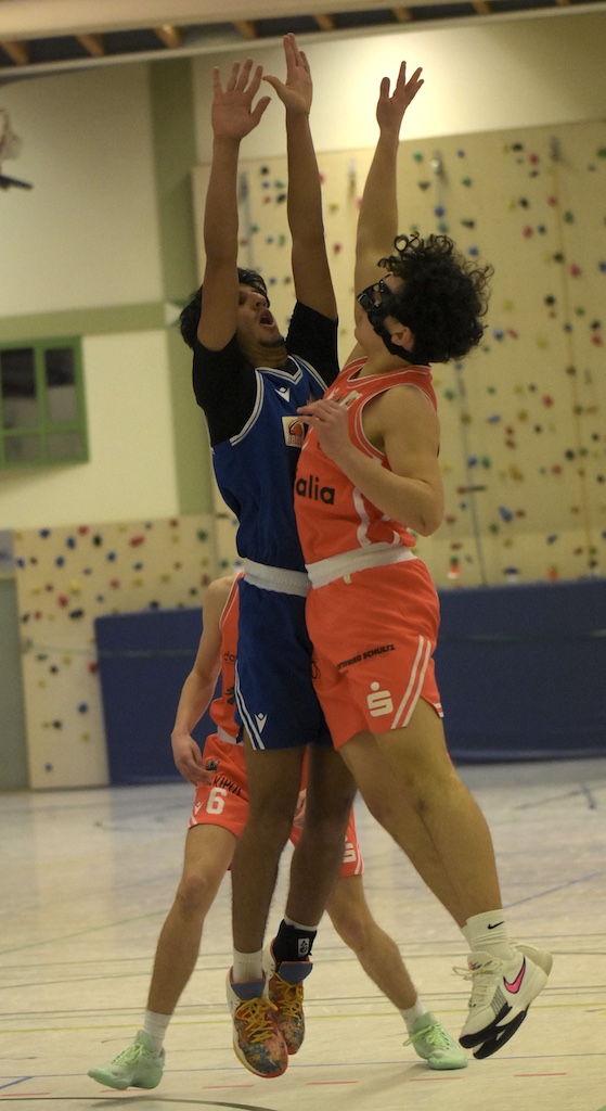 Zwei männliche Basketballspieler springen kämpferisch mit entschlossenen Gesichtern Richtung Korb