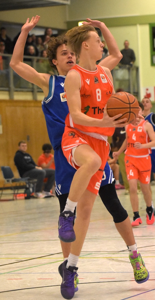 Zwei junge Basketballspieler, einer in orange, einer in blau, kämpfen dynamisch um den Ball