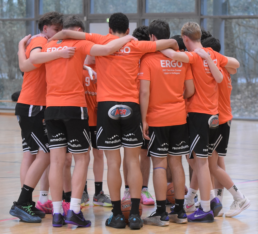 Eine Gruppe Jugendlicher in orangenen Trikots steht eng umarmt im Hallensport.