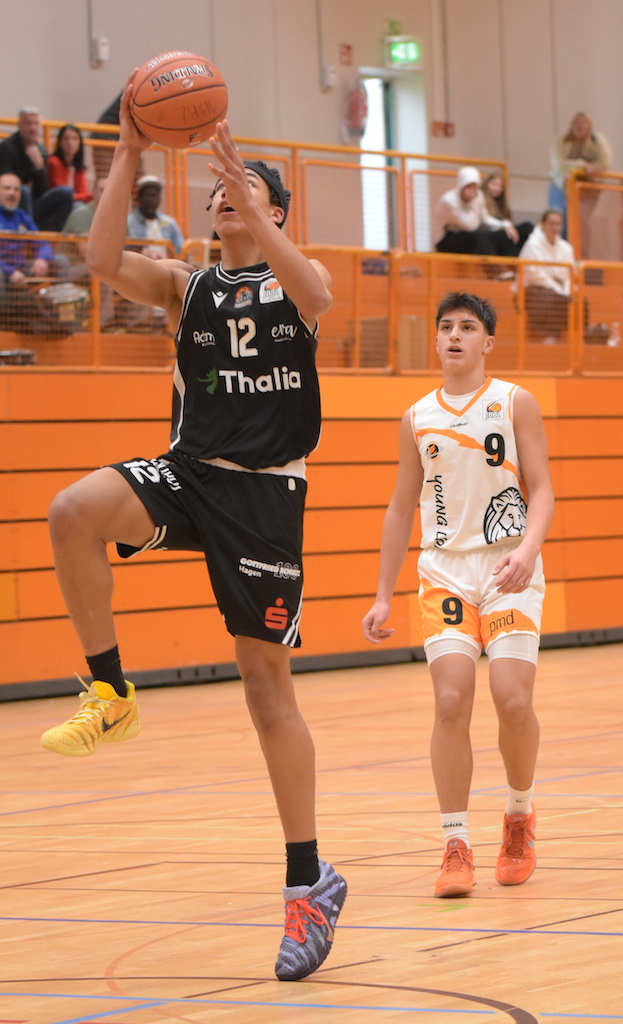 Ein junger Basketballspieler im schwarzen Trikot springt energiegeladen zum Korb