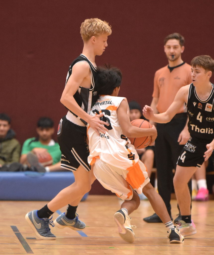 Ein Basketballspieler in einem weißen Trikot dribbelt an zwei Gegnern in Schwarz vorbei