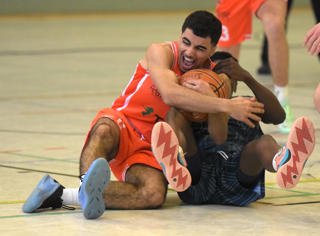 Ein lächelnder Basketballspieler im orangen Trikot kämpft auf dem Boden um den Ball
