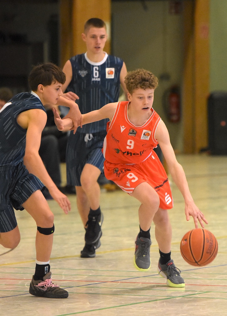 Ein Junge in orangefarbenem Trikot dribbelt konzentriert einen Basketball in der Halle