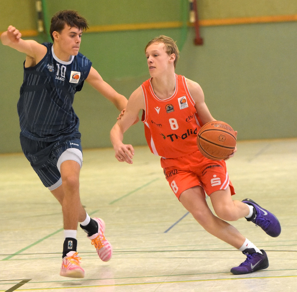 Zwei junge Basketballspieler, einer im blauen und einer im roten Trikot, kämpfen konzentriert um den Ball