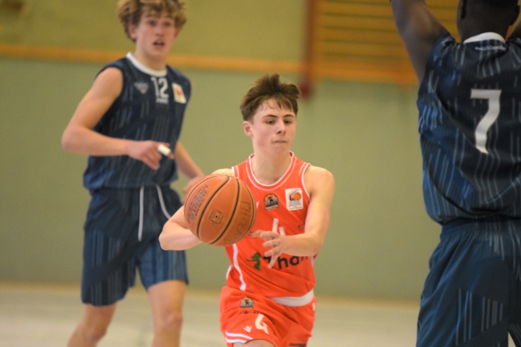 Ein junger Basketballspieler im orangefarbenen Trikot passt konzentriert den Ball